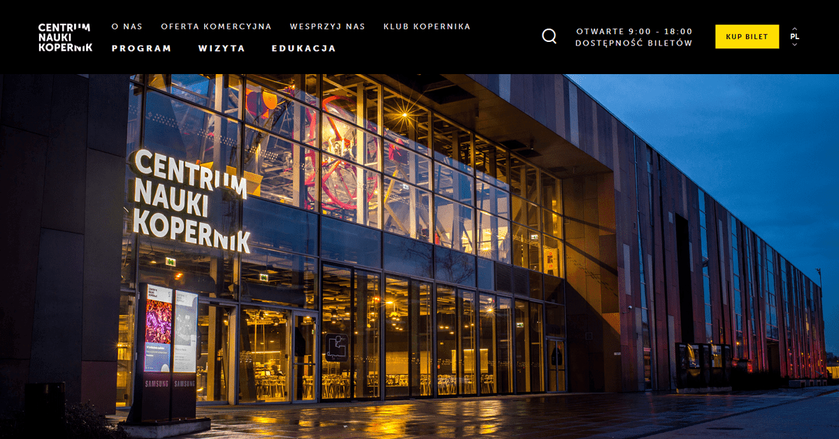 Wieczorny widok budynku Centrum Nauki Kopernik z podświetlonym wejściem.