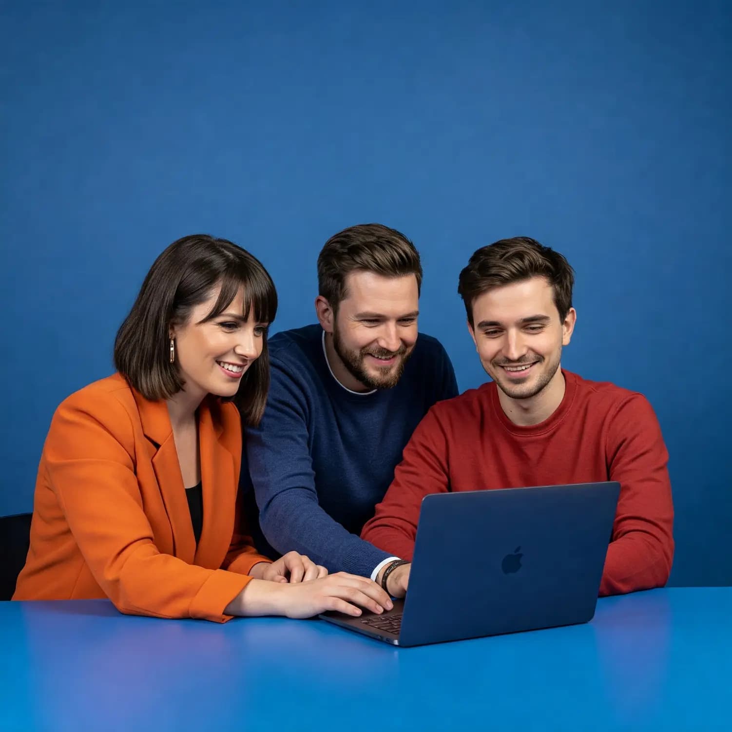 Trzy osoby w kolorowych stylizacjach współpracujące przy laptopie, symbolizujące kreatywny zespół projektowy IT