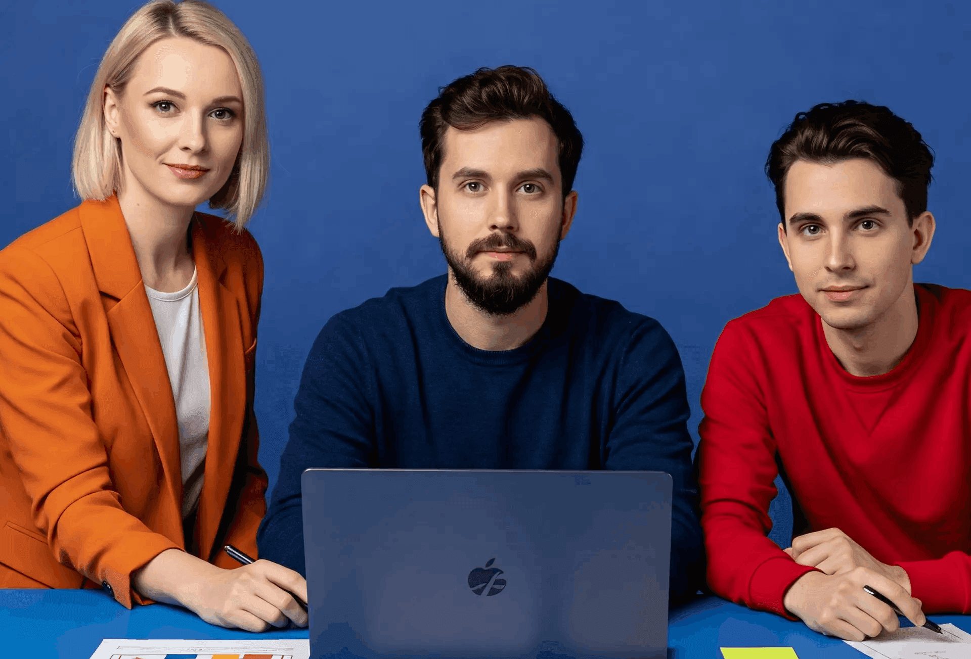 Trzyosobowy zespół specjalistów IT z Fabrity Digital współpracuje przy laptopie nad projektem cyfrowym, na tle niebieskiej ściany.