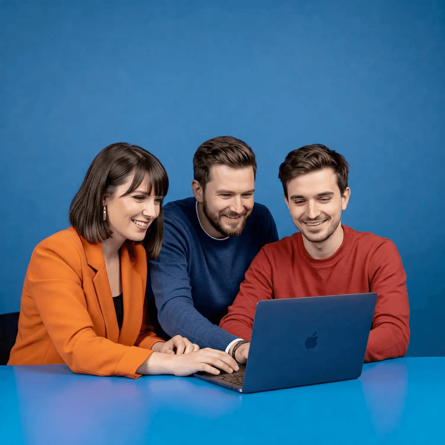 Trzy osoby w kolorowych stylizacjach współpracujące przy laptopie, symbolizujące kreatywny zespół projektowy IT