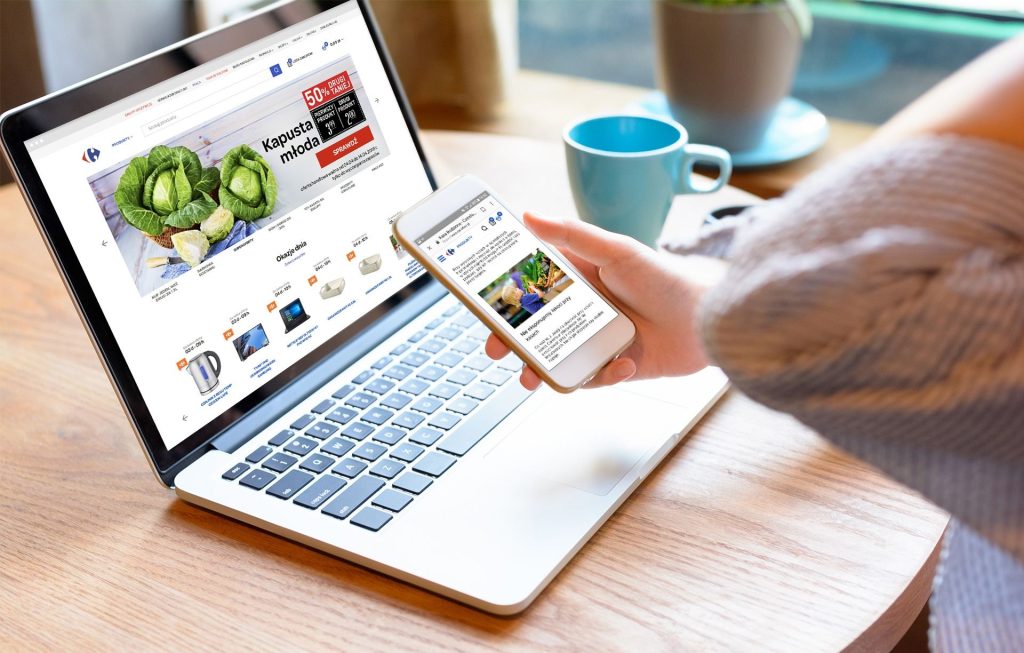 Osoba używa laptopa i smartfona z otwartym sklepem internetowym.